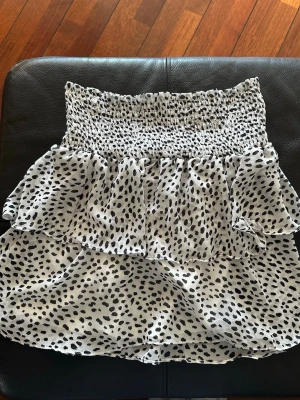 Vit/svart volangkjol från Chelsea - Supersöt kort volangkjol från Chelsea i vitt med svart leopardmönster. Kjolen har smock i midjan och dubbla volanger för en extra flowy känsla. Storlek m🐆🩶🪩