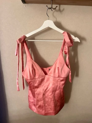Rosa korsettopp med knytband - Snygg rosa korsettopp med knytband på axlarna och v-ringad urringning. Använd vid något enstaka tillfälle! Så den är som ny. 
