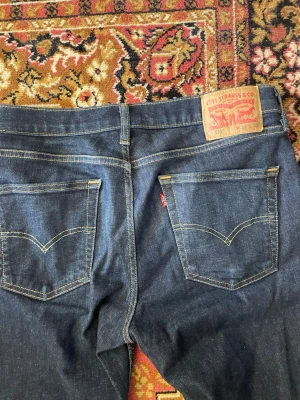 Mörkblå Levi's 511 jeans - Säljer ett par klassiska mörkblå Levi's 511 jeans med raka ben och snygga kontrastsömmar. Jeansen har två bakfickor med den ikoniska V-formade sömmen och en röd Levi's-tag. Tillverkade i slitstarkt denimtyg som passar till det mesta. 32/32!
