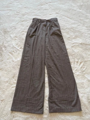 Bruna vida kostymbyxor - Säljer ett par bruna kostymbyxor med hög midja och vida ben. Byxorna har pressveck framtill, bälteshällor och stängs med hake och dragkedja. Materialet känns mjukt och har en diskret struktur som ger en klassisk look.Tags: Vintage nyc downtown skins parisian subversive alternative New York copenhagen style girly sex and the city Carrie Bradshaw scandi matilda djerf simple euro summer ballet carolyn bessette kennedy basics 90s y2k lana del ray bella hadid lili rose depp london archive classy retr