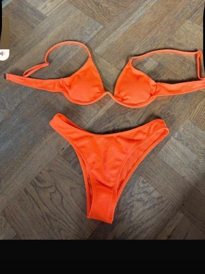 Orange bikini med struktur - Snygg orange bikini med strukturerat tyg och bygel-bh. Bikinitoppen har smala axelband och trosan har hög midja med en tight passform. Perfekt för stranden eller poolen i sommar!