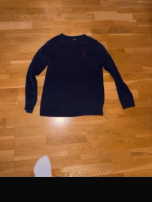 Mörkblå tröja från Ralph Lauren - Snygg mörkblå tröja från Ralph Lauren med den klassiska röda loggan broderad på bröstet. Tröjan har rund halsringning och långa ärmar. Perfekt för dig som gillar stilrena och tidlösa plagg.