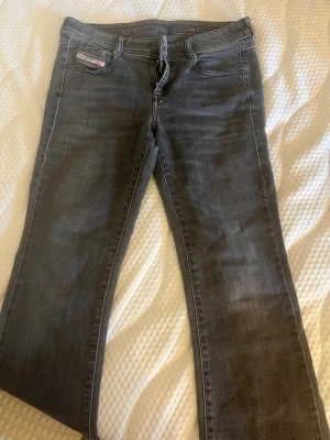 Mörkgrå jeans från Diesel - Säljer ett par mörkgrå jeans från Diesel med klassisk femficksmodell och raka ben. Jeansen har snygga slitningar och diskreta kontrastsömmar. Materialet är mjukt denim som sitter skönt och passar till det mesta. Perfekta för dig som gillar en avslappnad men stilren look. Dock har ett hål mellan benen går att sy ihop men har inte orkat riktigt!