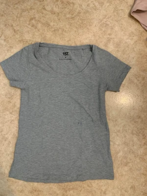grå basic t-shirt från 157 - En enkel och stilren grå t-shirt från 157 med rund halsringning och korta ärmar. Tillverkad i mjukt och stretchigt material som passar perfekt till alla typer av outfits. Klassisk passform och diskret design utan tryck.