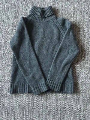 Mörkgrå polotröja stickad - Mysig mörkgrå stickad polotröja med ribbad krage, ärmslut och nederkant. Tröjan har lång ärm och enkel, stilren design som passar perfekt till kalla dagar. Materialet ser ut att vara mjukt och värmande, perfekt för höst och vinter. (Något liten i stl)