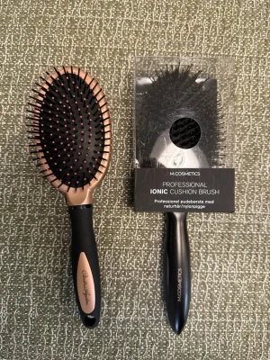 2 st paddelborstar för håret - Säljer två paddelborstar för håret. Ena borsten är svart och roséguld från Christina Aguilera med plastpiggar och mjukt grepp. Den andra är en svart M.COSMETICS Professional Ionic Cushion Brush med naturhår och nylonpiggar, fortfarande i förpackning.
