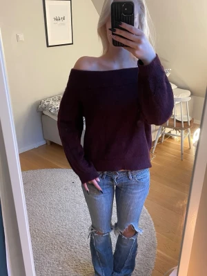 Vinröd off shoulder stickad tröja - Säljer en vinröd stickad tröja med off shoulder-modell och långa ärmar. Tröjan har en lös passform och är gjord i ett mjukt, fluffigt material som känns riktigt skönt mot huden. Perfekt för dig som vill ha en trendig och bekväm look.