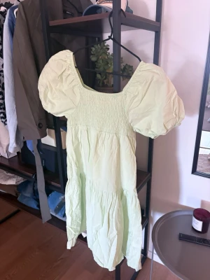 Ljusgrön klänning med puffärmar - Söt ljusgrön klänning med puffiga kortärmar och smockad överdel. Klänningen har en luftig passform och faller i flera lager för en romantisk look. Perfekt för varma dagar och somriga tillfällen.