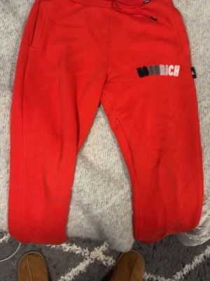 Röda mjukisbyxor från Hoodrich XS - Snygga röda mjukisbyxor från Hoodrich i storlek XS. Byxorna har broderad logga i svart, grått och vitt på ena benet och dragsko i midjan. Perfekta för chill eller träning, tillverkade i mjukt material för maximal komfort.