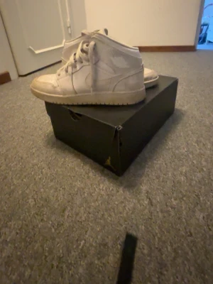 Vita Nike Air Jordan 1 Mid sneakers - Snygga vita Nike Air Jordan 1 Mid sneakers med klassisk siluett och ikoniska detaljer. Skorna har en högre profil, vita skosnören och gummisula med Air-dämpning. Tillverkade i läder och textil för en clean och sportig look.