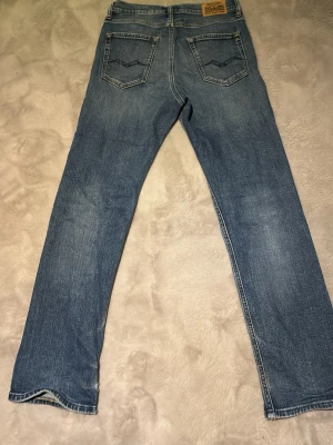 Blå raka jeans från Nudie Jeans - Säljer ett par klassiska blå jeans från replay Jeans med raka ben och två bakfickor med vågig söm. Jeansen har en ljus tvätt och är tillverkade i denim med en snygg vintagekänsla. Perfekta för en avslappnad och trendig stil.