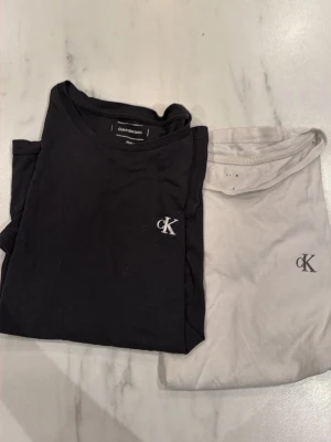 2-pack Calvin Klein t-shirts - Säljer två stilrena t-shirts från Calvin Klein Jeans, en svart och en vit. Båda har klassisk rund hals och diskret CK-logga broderad på bröstet. Perfekta basplagg i mjuk bomull som passar till allt.
