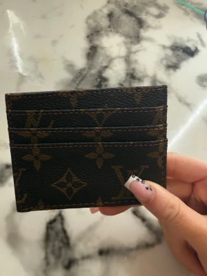 Louis Vuitton monogram korthållare - Snygg korthållare från Louis Vuitton i klassiskt brunt monogrammönster. Tillverkad i tåligt canvasmaterial med plats för flera kort. Slimmad och smidig design som enkelt får plats i fickan. Perfekt accessoar för dig som gillar lyxiga detaljer.