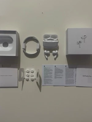 Apple AirPods Pro med laddningsetui - Säljer ett par vita Apple AirPods Pro med trådlöst laddningsetui. Hörlurarna har en stilren och kompakt design i plast, silikonproppar i olika storlekar och kommer med originalkartong, laddkabel och manualer. Perfekta för dig som vill ha grymt ljud och smidig anslutning.