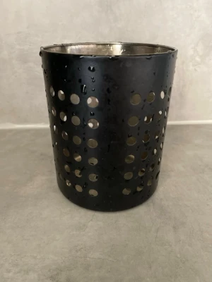 Svart bestickställ i metall - Säljer ett svart cylinderformat bestickställ i metall med hålmönster runt om. Perfekt för att förvara bestick eller köksredskap på ett stilrent sätt. Enkel design som passar i de flesta kök.