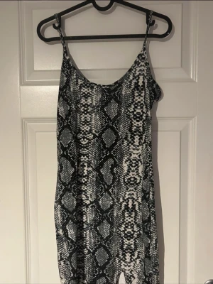 Svartvit ormmönstrad klänning med slits - Kort svartvit klänning med trendigt ormmönster och smala axelband. Liten slits framtill som ger extra edge och en snygg siluett. Mjukt och stretchigt material som formar sig fint efter kroppen🐍🔥(ifrån shein) 