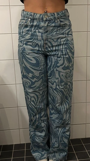 Blå mönstrade jeans med swirlmönster - Unika blå jeans med swirlmönster i ljusblått och mörkblått. Modellen har raka ben och hög midja, vilket ger en trendig och avslappnad look. Jeansen är tillverkade i klassisk denim och har fickor både fram och bak. Perfekta för dig som vill sticka ut!