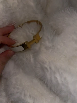 H-armband - Snyggt armband från H i guldtonad metall med vit emalj och ikonisk H-formad detalj framtill. Stilren och modern design som ger en lyxig touch till din outfit. Perfekt för dig som gillar exklusiva accessoarer. Köpt i Grekland därav inte äkta.