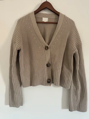 Beige ribbstickad kofta med knappar - Säljer en beige ribbstickad kofta med tre stora knappar framtill och  V-ringning. 
