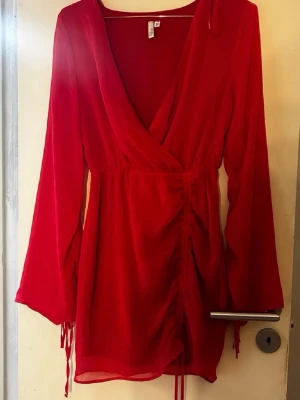 Röd omlottklänning med snörning - Trendig röd kortklänning från Nelly med omlottmodell och v-ringning. Klänningen har långa ärmar och snörningsdetalj framtill som ger en snygg siluett. Perfekt för dig som vill sticka ut med en färgstark look.  Endast testad, nypris 699kr