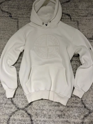 Vit hoodie Stone Island - Säljer en stilren vit hoodie från Stone Island med broderad logga på bröstet. Hoodien har en klassisk känguruficka, ribbade muddar och dragsko i huvan. Perfekt för dig som gillar streetwear och vill ha något enkelt men ändå exklusivt.
