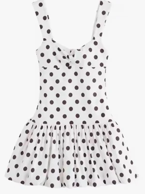 Vit prickig kortklänning med rosett - Supersöt vit kortklänning med svarta prickar och en liten rosettdetalj framtill. Klänningen har breda axelband och en utställd kjol som ger en lekfull vibe. Perfekt för varma dagar när du vill känna dig extra gullig.