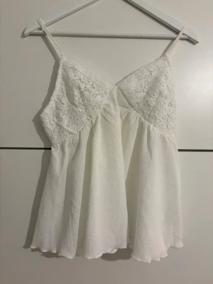 Vit spetslinnetopp från SHEIN - Säljer en söt vit linnetopp från SHEIN med tunna axelband och spetsdetaljer över bysten. Toppen har en flowy passform och är tillverkad i ett lätt material som känns luftigt och fräscht. Perfekt för varma dagar eller som layering-piece.