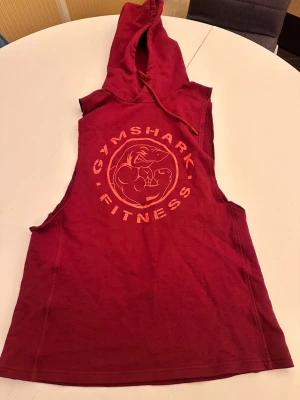 Svart t-shirt från Gant - Snygg röd ärmlös hoodie från Gymshark med stort tryck på bröstet. Perfekt för gymmet eller träning, med huva och dragsko. Materialet känns mjukt och lätt, och passformen är loose för maximal rörelsefrihet.