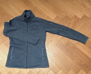 Blå fleecejacka från Patagonia - Mysig blåmelerad fleecejacka från Patagonia med hel dragkedja, hög krage och två fickor framtill. Ärmen har en extra ficka med dragkedja. Perfekt för lager-på-lager och outdoor-vibes.