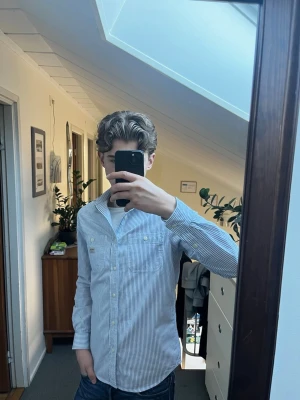 Randig skjorta från Ralph Lauren Denim & Supply - Säljer en klassisk vit skjorta med tunna blå ränder från Denim & Supply Ralph Lauren. Skjortan är tillverkad i 100% bomull och har långa ärmar samt knappar framtill. Perfekt för en stilren och avslappnad look.