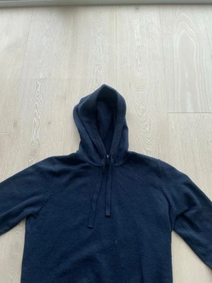 Mörkblå hoodie från RYVLS Stockholm - Mörkblå hoodie från RYVLS Stockholm med klassisk huva och dragsnören. Tillverkad i mjukt material som känns skönt mot huden. Perfekt för dig som gillar en enkel och stilren look. Passar till det mesta och är lätt att matcha med andra plagg. Allt ul på tröjan kan man tar bort med tvätten eller rullband