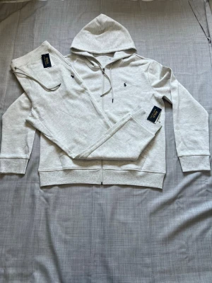 Ralph lauren tracksuit grå strl L - Helt ny Ralph Lauren tracksuit säljes med hoodie och byxor. Väldigt clean och bekvämt set som passar perfekt till vardag och resor. Sjukt populär modell och riktigt bra passform. Oanvänd i storlek L. Snabb frakt och paketpris finns 🔥