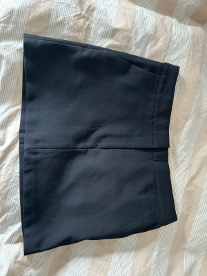 Svart kortkjol i klassisk modell -  svart kortkjol med rak passform och diskreta fickor bak. Kjolen har en enkel design utan mönster och är perfekt för en clean och snygg look. Tyvärr bara för stor så därför säljer jag den