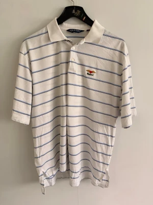 Polo Ralph Lauren piké - • 🇸🇪 Vit (m. Blåa ränder) GolfPiké från Polo Ralph Lauren. Broderad logga på bröstet.   Använd, men fortfarande i fräscht skick utan några speciella anmärkningar.  Väldigt schysst och lent material, golf anpassat.  *Den har ett litet hål, syns på sista bilden*  Pris går alltid att diskutera vid snabb affär 🥂
