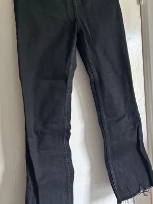 Svarta utsvängda jeans från Zara - Säljer ett par svarta jeans från Zara med rak passform och råa, fransiga benslut. Jeansen har klassisk femficksdesign och dragkedjegylf. Tillverkade i ett mjukt denimtyg som är bekvämt att bära. Perfekta för en avslappnad och trendig look.
