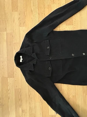  overshirt  - Stilren blå svart overshirt från A Day's March med två stora bröstfickor med lock och knappar framtill. Klassisk krage och raka ärmar. Perfekt lager-på-lager-plagg i ett mjukt, tjockare tyg som ger en clean look. Saknar en knapp men går enkelt att fixa 