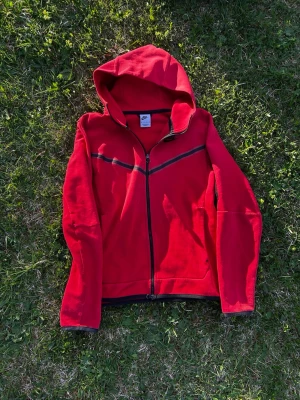 Nike tech tröja - Säljer nu en röd nike tech tröja. Den är väl använd och jag visar även defekterna på den på bilderna. Pris är inte hugget i sten. Jag har xs vanligtvis, men denna sitter mer som S, så är du runt 170 och lite över bör den passa perfekt. 