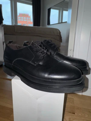 Massimo Dutti derby chunky soles dress shoes. - Säljer ett par svarta loafers med chunky sula och snörning. Skorna är tillverkade i slätt läder och har en stilren, minimalistisk design som passar till många olika outfits. Perfekta för dig som gillar en modern och clean look.Massimo Dutti derby chunky soles dress shoes. Endast använda en gång