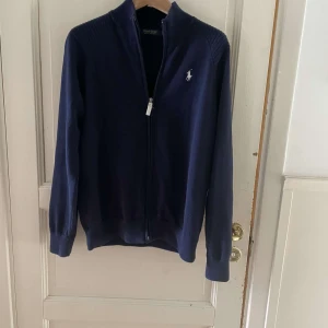 Ralph lauren full zip - Säljer en stilren mörkblå kofta från Polo Golf Ralph Lauren. Tröjan har hel dragkedja framtill, ribbade muddar och en broderad logga på bröstet. Perfekt för lager-på-lager och passar till många tillfällen.
