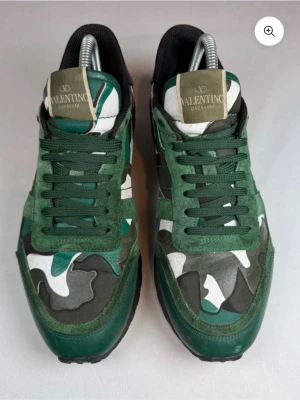 Valentino Garavani Rockrunners ”camo sneakers’’ - Snygga sneakers från Valentino Garavani med grön, svart och vit camo-mönstrad ovandel. Skorna har gröna skosnören, med en svart häl och detaljer i mockan men ochså läder. Perfekta för dig som gillar streetwear. Och vill ha en trendig och stilren look i vardagen. 