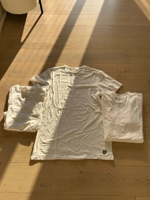 3 pack vita t-shirts från Lyle & Scott - Tre vita t-shirts från Lyle & Scott med klassisk passform och rund hals. En av tröjorna har den ikoniska Lyle & Scott-loggan i form av en gul fågel på nederkanten. Perfekta basplagg till garderoben. Är lite skrynkliga men är faktiskt använda pågrund av att dom är förstora.