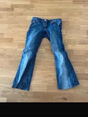 Blå bootcut jeans från Gina Tricot - Säljer ett par blå bootcut jeans från Gina Tricot i storlek 170. Jeansen har klassisk femficksmodell, röda sömmar och lätt slitna detaljer framtill. Perfekta för dig som gillar en retro och avslappnad look. trasig lite men är också förkortad vid benen 
