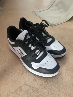 Svarta och vita sneakers Tommy Jeans - Snygga sneakers från Tommy Jeans i svart och vitt läder med klassisk låg siluett. Skorna har perforerad tå, svarta snören och tydlig logga på sidan. Perfekta för dig som gillar streetwear och vill ha en clean look. Använts två gånger 