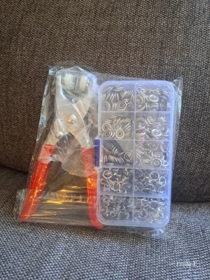 Tång med tryckknappar  - Praktiskt kit med tång och flera fack med silverfärgade öljetter och ringar, perfekt för att skapa eller laga smycken. Tången har röda handtag och medföljer gör en plastlåda med sorterade metalldelar. Perfekt för dig som gillar DIY och pyssel.