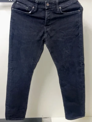 Svarta jeans från Jack and Jones  - Snygga svarta jeans med hög midja och smal passform. Klassisk femficksmodell med knapp och dragkedja framtill. Perfekta till sneakers eller boots och funkar året runt. Materialet känns mjukt och stretchigt för extra komfort.