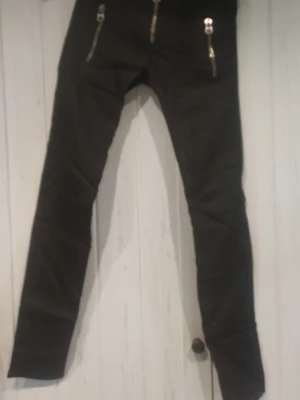Svarta skinny jeans med dragkedjor - Säljer ett par svarta skinny jeans med tre snygga dragkedjor framtill. Jeansen har smal passform och är tillverkade i ett stretchigt material som sitter tajt längs benen. Perfekta för dig som gillar en edgy och modern stil.