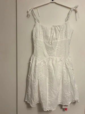 Vit kort klänning - Superfin vit kortklänning med broderade blommor och knytband vid axlarna. Klänningen är perfekt till skolavslutning, student osv men även bara till en vanlig sommardag. Från cider och är aldrig använd med lapparna kvar. 