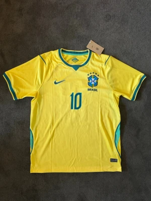 Brasilien VM 26/27 hemma Neymar Jr 10  - Fotbollströja med Neymar JR på ryggen. Tröjan är helt ny med tagg kvar och i perfekt skick. Storlek M. Perfekt för dig som är supporter, samlar på fotbollströjor eller vill ha en snygg tröja till träning och vardag. 🟨 Storlek M 🟨 Helt ny med tagg 🟨 Neymar JR 🟨 Skickas inom 24 timmar Vid intresse eller frågor är det bara att skicka 👍