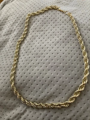 Guldfärgat tvinnat halsband - Snyggt guldfärgat halsband med tvinnad kedja som ger en cool och trendig look. Halsbandet har en klassisk karbinhake och passar perfekt för att lyfta vilken outfit som helst. Materialet ser ut att vara metall med glansig finish.