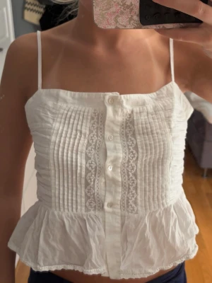 Vit topp - Söt vit linnetopp från Zara med tunna axelband, knappar framtill och dekorativa spetsdetaljer. Perfekt för varma dagar och enkel att styla till jeans eller kjol. Endast använd ett fåtal gånger och varnings skavanker🥰